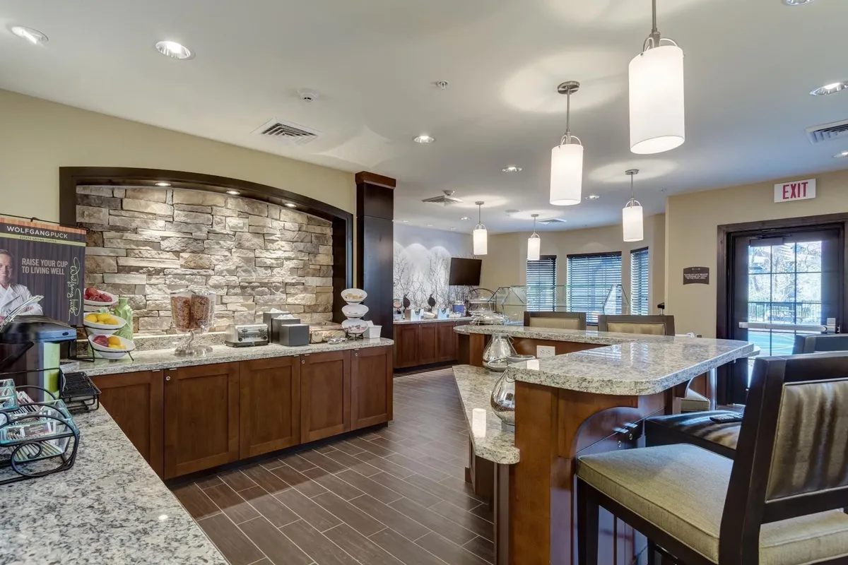 A welcoming breakfast area with a granite countertop, stone wall, comfortable seating, and a breakfast buffet setup. Guests are shown enjoying breakfast, chatting, and starting their day in a relaxed environment.