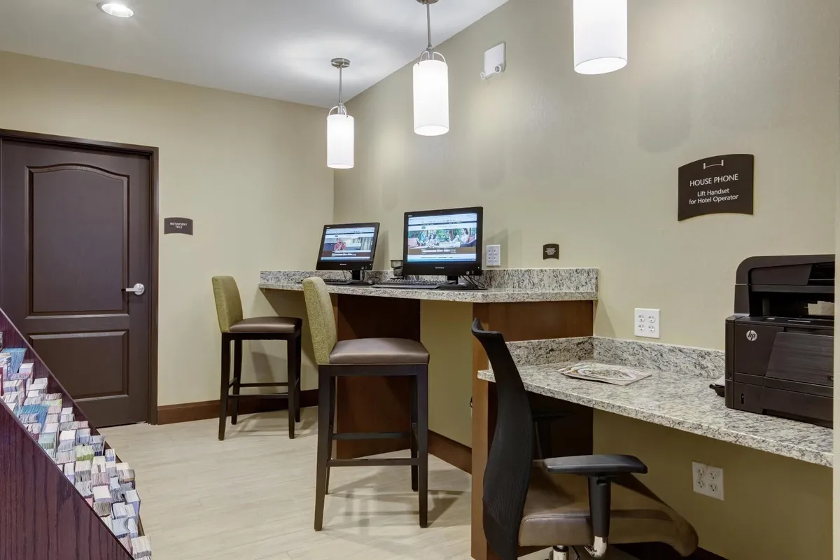 A modern business center with computer stations set along a granite countertop, illuminated by pendant lighting. The setup is practical and sleek, designed for productivity whether guests need to print documents or plan their day.