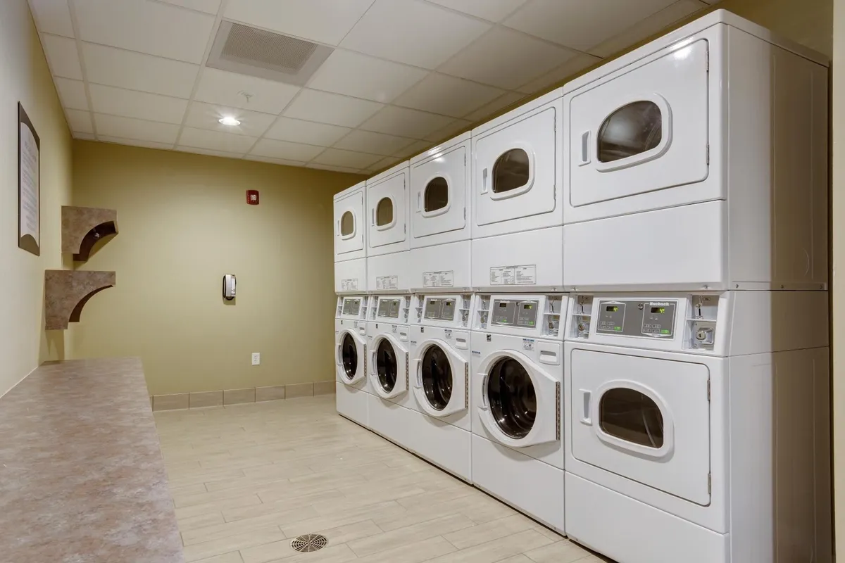 A well-organized laundry facility featuring stacked washers and dryers, a practical countertop for folding clothes, and wall-mounted shelving for supplies. The space is orderly and bright, emphasizing ease of use and convenience for guests needing to do laundry during their stay.