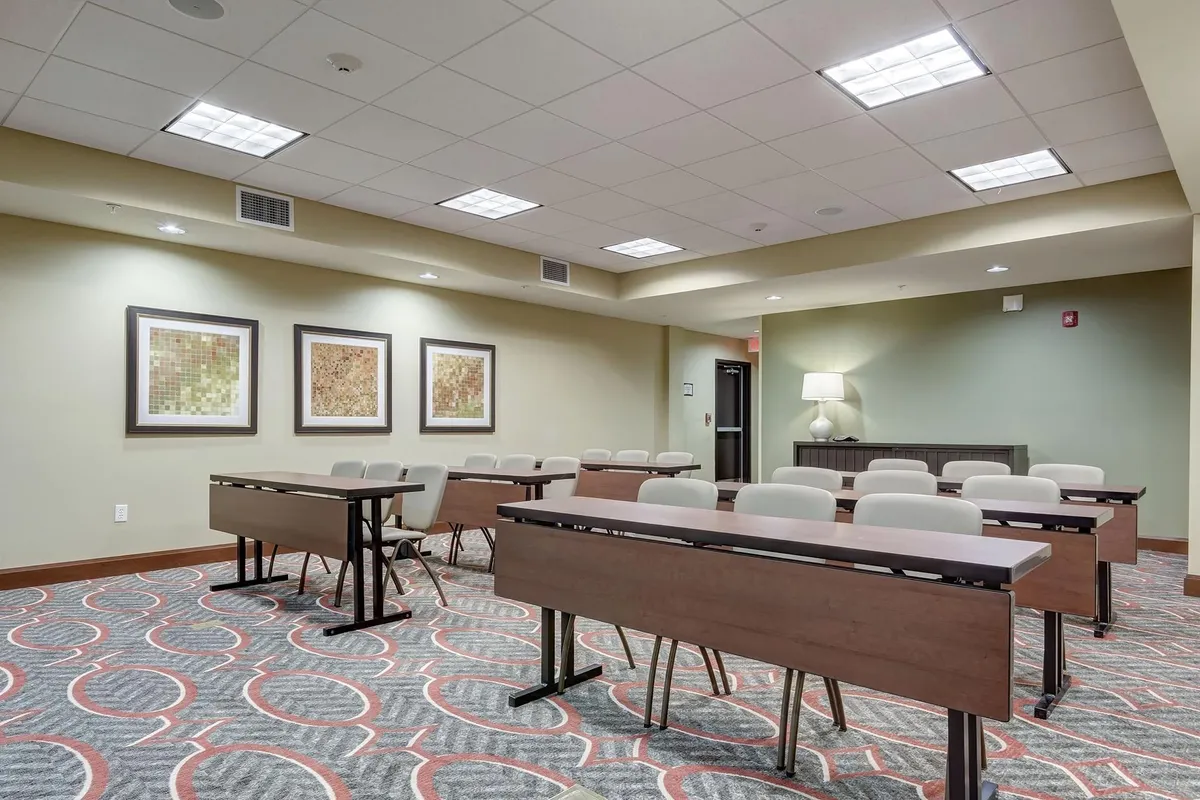 A thoughtfully arranged meeting space featuring classroom-style tables, comfortable chairs, and decorative artwork on the walls. The room is set up for collaborative work or small group sessions, with plenty of natural light and a welcoming, professional ambiance.
