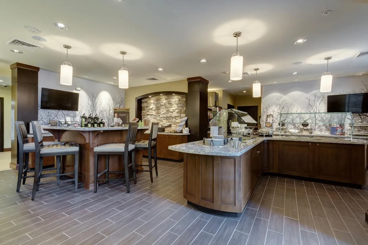 This image showcases a modern interior space featuring a wooden bar counter, granite serving station, stone accent wall, and a seating area with bar stools. The setting is perfect for casual dining, enjoying coffee, or gathering with friends and family.