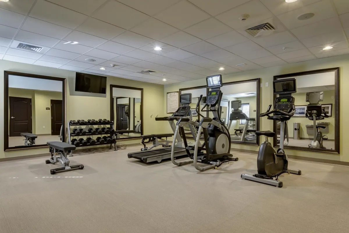 A bright and invigorating fitness center equipped with modern exercise machines, a dumbbell rack, and full-length mirrors. The space is clean, well-lit, and inviting, ideal for unwinding or maintaining fitness routines while on the road.