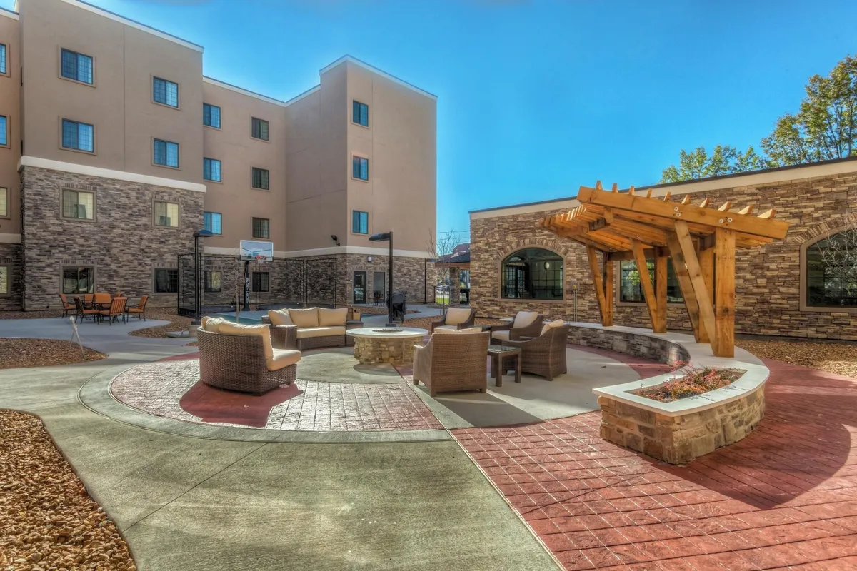An exterior communal space featuring a cozy outdoor seating area with a fire pit, wooden pergola, and stone walls. The mood is relaxed and communal, perfect for families to gather, socialize, or unwind after a day of exploring local attractions.