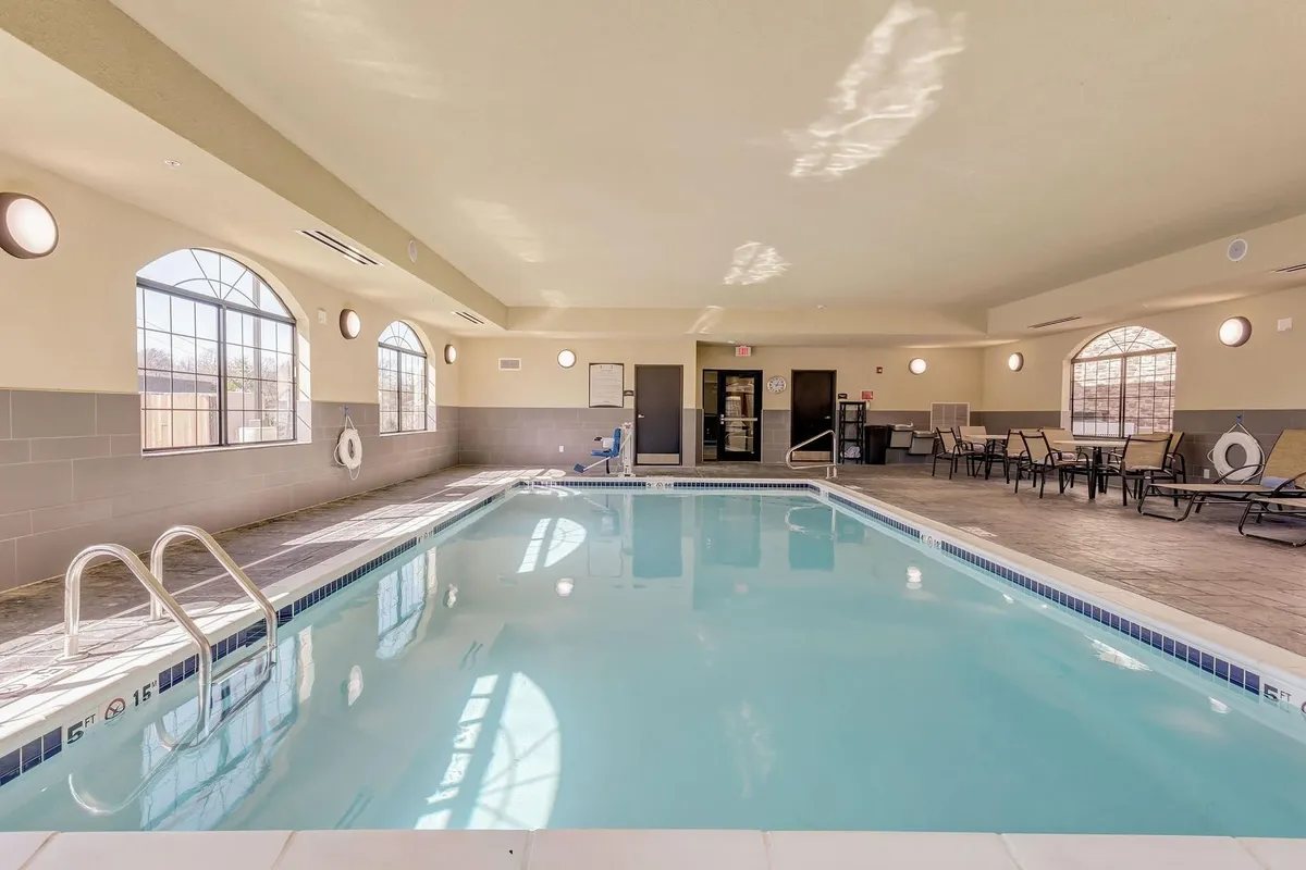 This image features a bright indoor swimming pool surrounded by lounge chairs and large windows that let in natural light. The setting is inviting, offering a tranquil space for relaxation and gentle recreation. The view emphasizes both the comfort of the pool area and its potential as a peaceful retreat.
