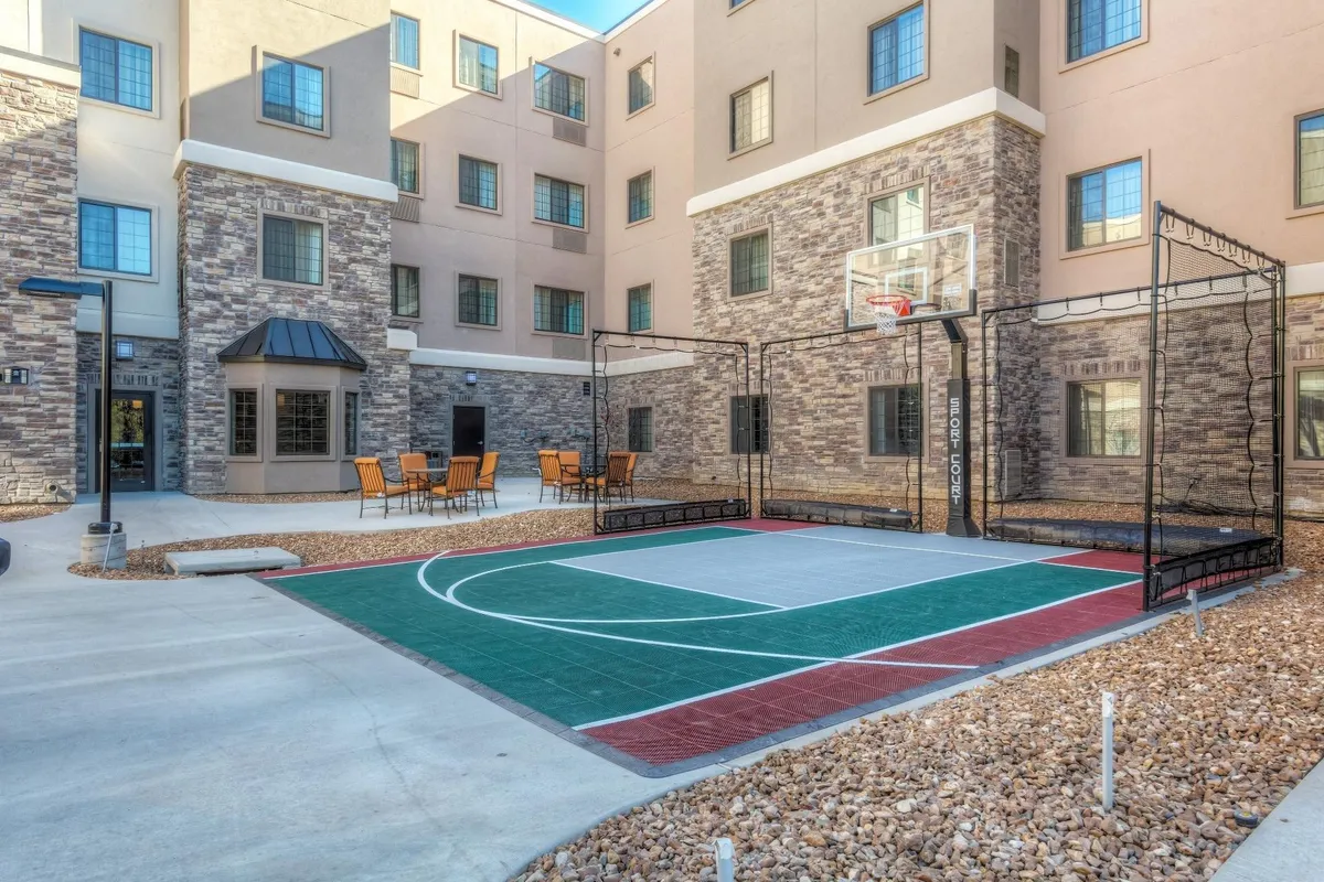 This exterior image features a vibrant basketball court adjacent to a patio seating area, with the hotel building facade in the background. The scene is lively, suggesting spaces for energetic play and outdoor family fun, with plenty of room for socializing and relaxing in the sunshine.