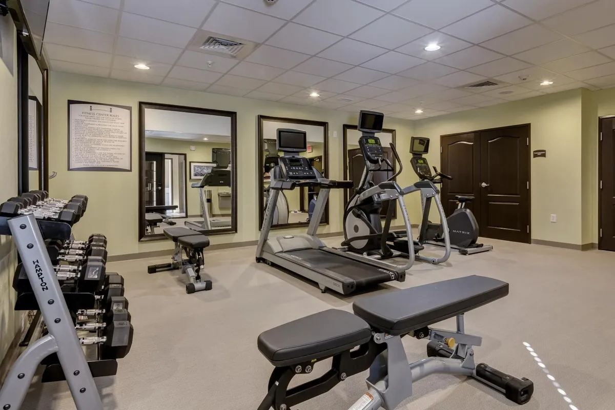 A well-equipped fitness center featuring treadmills, elliptical machines, free weights, and bright mirrored walls. The vibrant environment is ideal for guests seeking to maintain their workout routines at any hour.
